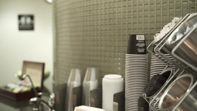Someone getting a cup and a napkin to serve himself with some coffee out of a coffee machine.