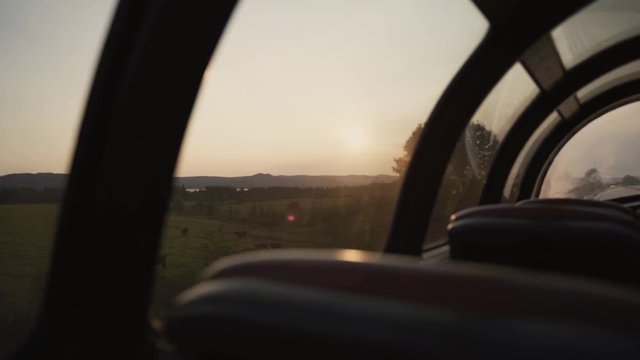 Farms, fields, landscapes and a small city seen from a sightseeing train (the seats of the train are also shown) - panoramic view during sunrise - slow motion.