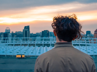 Fototapeta premium The guy looks at the sunset in the city