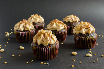 Set of chocolate cupcakes with peanut cream and chocolate sauce decorated with peanut on black background