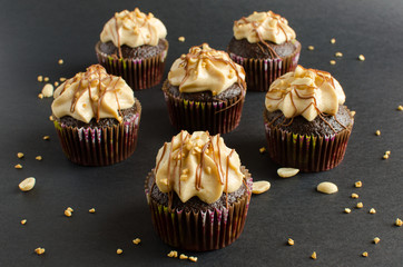 Set of chocolate cupcakes with peanut cream and chocolate sauce decorated with peanut on black background