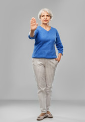 gesture, prohibition and old people concept - portrait of senior woman in blue sweater showing stop sign over grey background