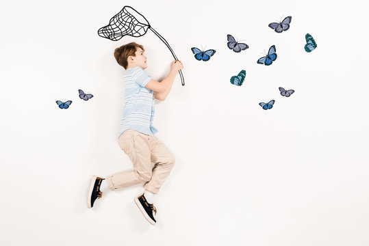 top view of cheerful kid holding butterfly net near butterflies on white