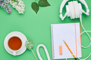 top view of the table of a teenage child, composition headphones notebook pencil flower drink Lollipop eraser on light green background