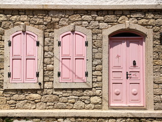 Tür und Fensterläden in Rosa einer Fassade aus hellem Naturstein und Bruchstein bei Sonnenschein...