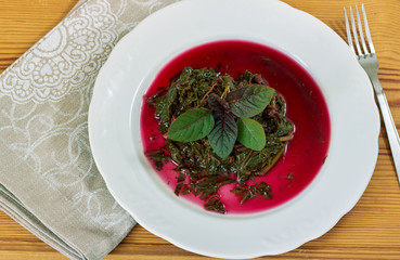 Prepaired braised amaranth - red spinach, in it's own sauce and a fresh leaf on top on white plate on wooden table  with linen napkin and fork nearby, copy space, close up, top view,