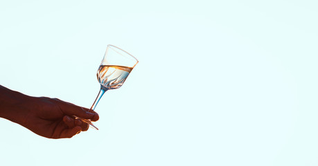 Male hand holding wineglasses with white wine over blue sky background
