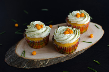 Set of cupcakes with yellow berries on wooden plank decorated with rosemary on black background