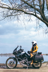 Biker girl wearing a motorcycle outfit, protective clothing, equipment, adventure touristic motorbike with side bags. outdoor travel, active traveler, lake and clouds. Vertical photo