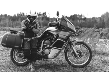 Fototapeta na wymiar Biker girl wearing a motorcycle outfit, protective clothing, equipment, adventure touristic motorbike with side bags. outdoor travel, active traveler, enduro, off road, blaack and white