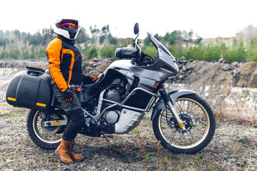 Fototapeta na wymiar Biker girl wearing a motorcycle outfit, protective clothing, equipment, adventure touristic motorbike with side bags. outdoor travel, active traveler, enduro, off road