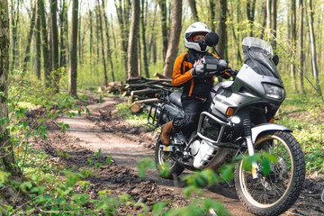 Fototapeta na wymiar Biker girl wearing a motorcycle outfit, protective clothing, equipment, adventure touristic motorbike with side bags. outdoor travel, off road enduro active traveler, sunny forest