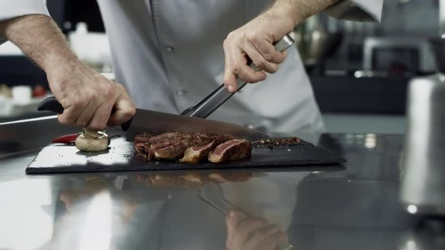 Male chef cutting steak at kitchen restaurant. Closeup chef hands cutting meat