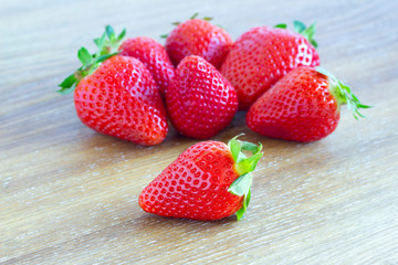 Strawberry in a group, one of them isolated closeup and focused on the wooden background table.