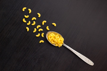 italian raw pasta horns dry on a metallic spoon and an black table