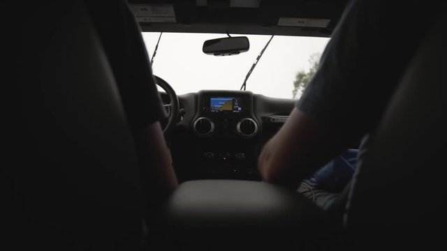 Shot taken from a back seat (low angle) of a Jeep car showing two men (arms only) on the front seats and a foggy / rainy day outside along the road - slow motion.