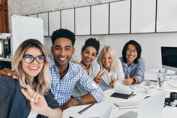 Blissful black man in checkered shirt gently embracing female colleague. Excited young workers of...