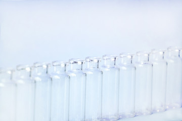 Empty glass medical vials, ampoules in a row on a light blue background with space for text. Glass medical bottles with selective focus. Vaccines, Medicine, Laboratory, Immunization concept.