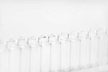 Empty glass medical vials, ampoules in a row on a light gray background with space for text. Glass medical bottles with selective focus. Vaccines, Medicine, Laboratory, Immunization concept.