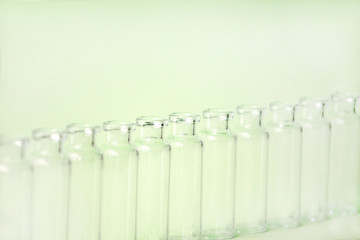 Empty glass medical vials, ampoules in a row on a light greenbackground with space for text. Glass medical bottles with selective focus. Vaccines, Medicine, Laboratory, Immunization concept.