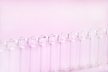 Empty glass medical vials, ampoules in a row on a light pink background with space for text. Glass medical bottles with selective focus. Vaccines, Medicine, Laboratory, Immunization concept.