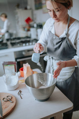 A middle aged woman pastry chef or baker preparing a cake and puts flour in a bowl.