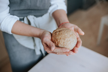 A middle aged crop woman in an apron holding a ball of dough for cooking.