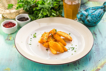 Baked unpeeled potato wedges on white plate on blue wooden table