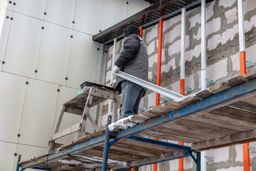 A worker installs a metal profile on the walls of a siding house