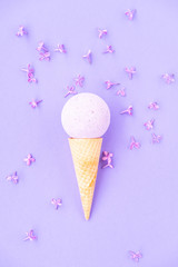 Composition of ice cream cone with bath ball on a violet background. Bathroom cosmetic accessories. Flat Lay. Top View. Lilac flowers