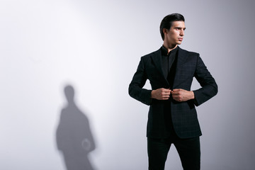 Obraz na płótnie Canvas A side image of elegant business man in black suit, arranjens his jacket, looks sideways, isolated on a background.