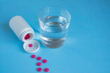 Bottle with pink pills and a glass of water on a blue background. Concept medicine, health, pharmacology. Free space for text