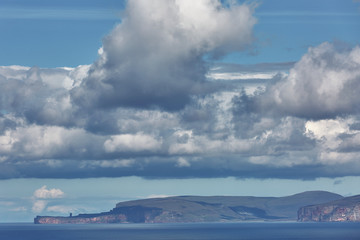 Orney cliffs with dramatic sky seen from John o'Groats over Atlantic ocean.