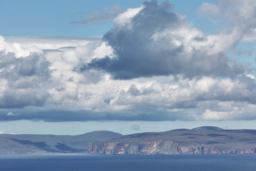 Orney cliffs with dramatic sky seen from John o'Groats over Atlantic ocean.