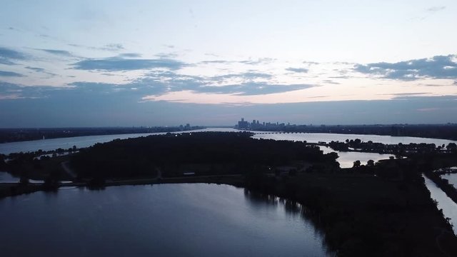 Belle Isle Detroit aerial view at sunset on a summer day. Bridge, buildings, boats visible in the distance. Island silhouette on the Detroit river with the Detroit skyline in the background.