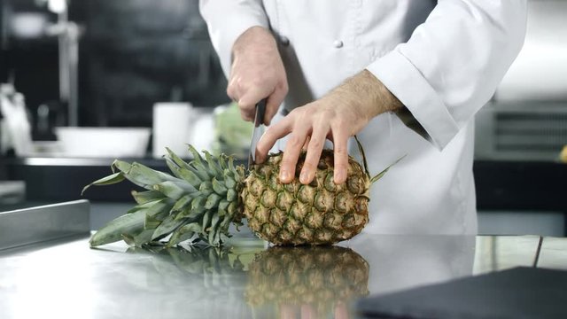 Chef chopping pineapple in slow motion. Man chef cutting fresh fruit.