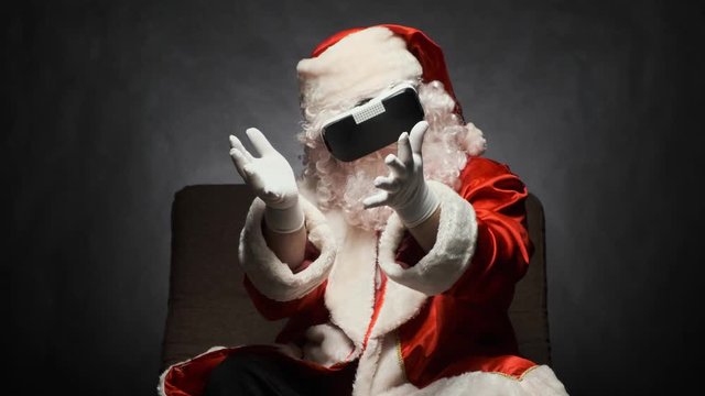 Santa Claus is having fun with glasses of virtual reality sitting in a chair on a black background