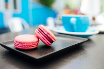 Obraz na płótnie Canvas Sweet, fresh macarons with coffee in a blue cup on a black table