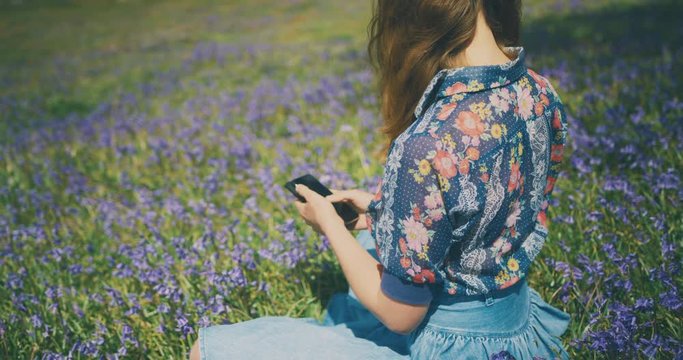 Young woman using smartphone in field of bluebells