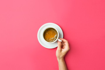 Young caucasian woman hands holds white cup with freshly brewed coffee with foamy crema on saucer on gradient fuchsia pink background. Trendy minimalist funky style