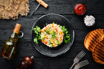 Boiled rice and vegetables. Risotto In a black plate. Top view. Free copy space.