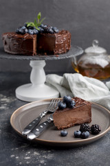 Piece of chocolate cake with whole cake behind on gray background
