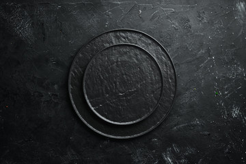 Round black stone plate. On a black stone background. Top view. Free space for your text.