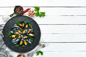 Obraz na płótnie Canvas Boiled mussels with parsley and spices on a black plate. Top view. Free space for your text.