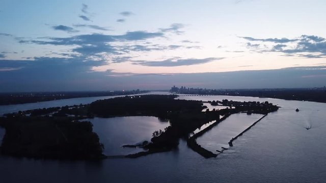 Belle Isle Detroit aerial view at sunset on a summer day. Bridge, buildings, boats visible in the distance. Island silhouette on the Detroit river with the Detroit skyline in the background.