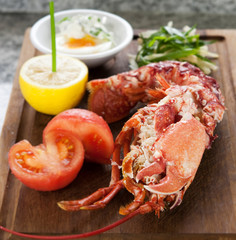 Whole cooked lobster served on rustic wooden board with tomato, lemon and poached egg.