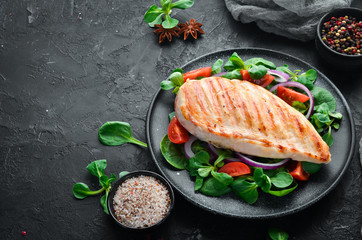 Baked chicken fillet with vegetables. In a black plate on a wooden background Top view. Free space...