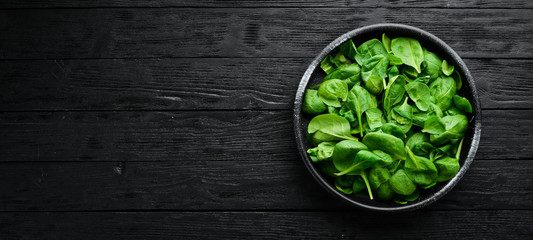 Fresh spinach. In a black plate on a wooden background Top view. Free space for your text. Flat lay