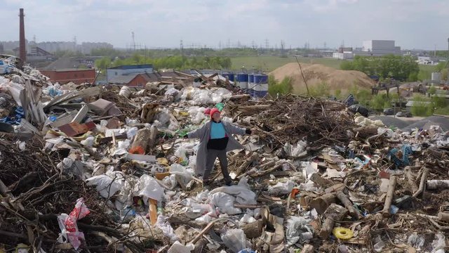 Aerial shot of tramp woman standing at peak of city dump mountain. homeless person is happy on trash mount.