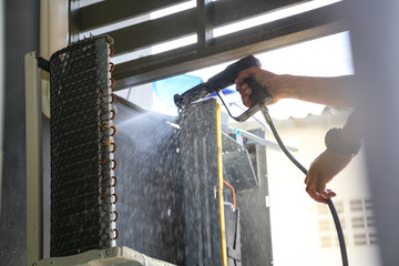 Technician cleaning air conditioner with water spray.
